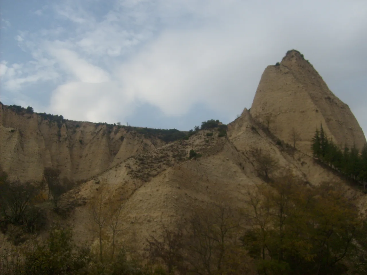 A tall pointed sandstone pyramid rising above eroded ridges near Melnik under a cloudy sky