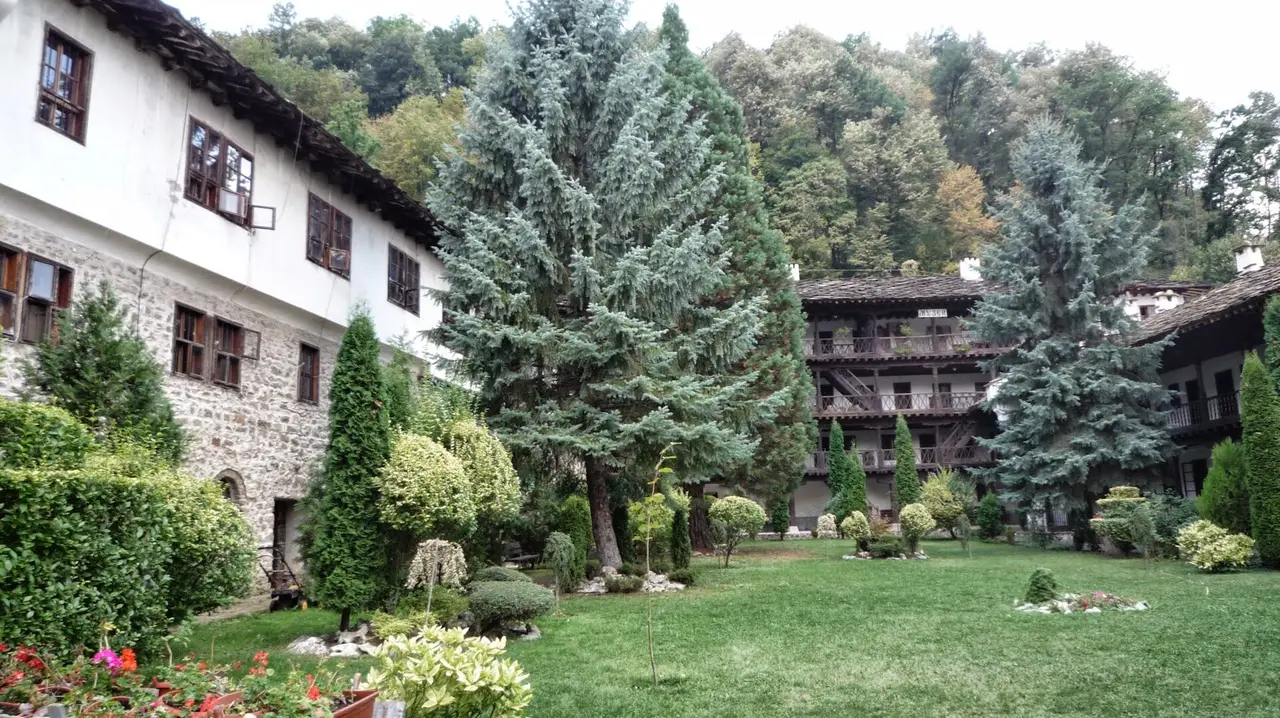 The wooden galleries and stone wings of Troyan Monastery around its green courtyard with tall spruces