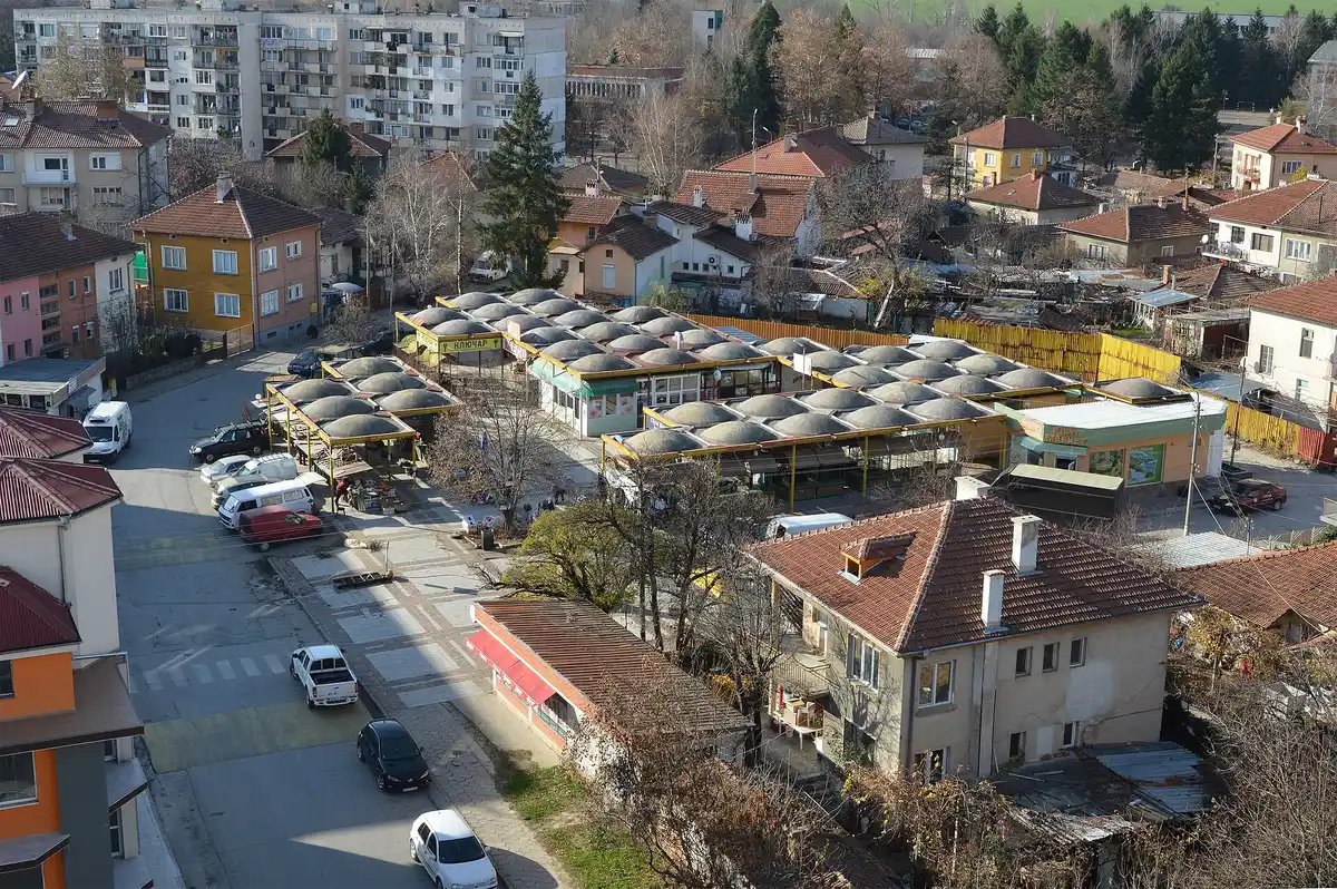 Aerial view of a small Bulgarian town, a market of domed-roof stalls beside apartment blocks and red-roofed houses with wooded hills behind