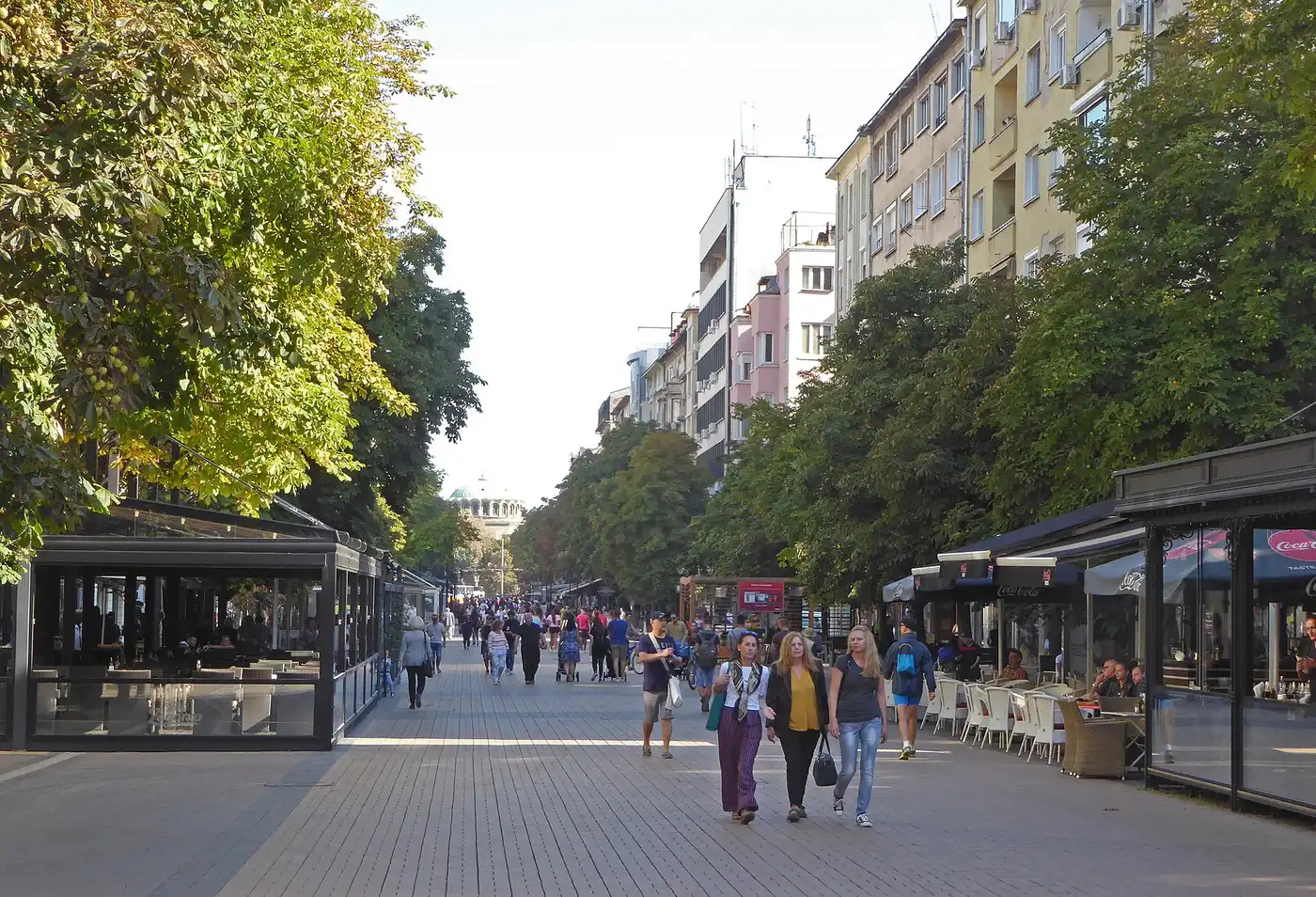 Pedestrians and cafe terraces along Vitosha Boulevard in central Sofia, tables under awnings on both sides of the tree-lined street on a sunny afternoon