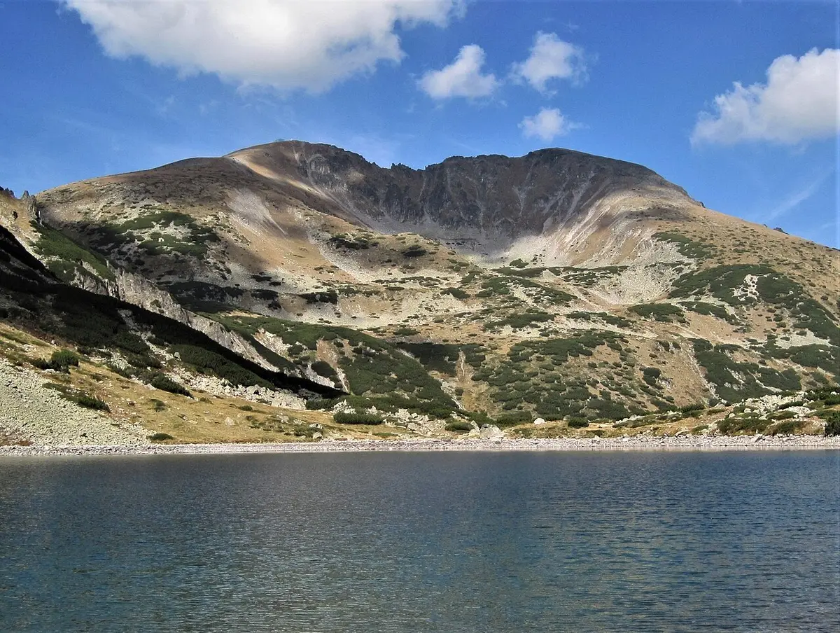 The twin rocky summits of Musala and Malka Musala seen across a mountain lake in the Rila range under a partly cloudy sky