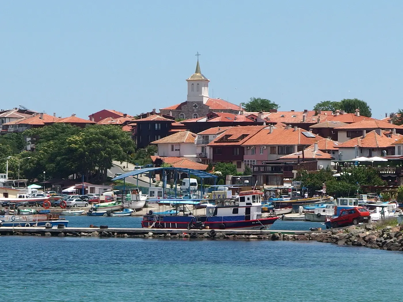 The red-roofed peninsula of Nessebar old town seen from the harbour, a church tower rising above the houses with fishing boats moored in front
