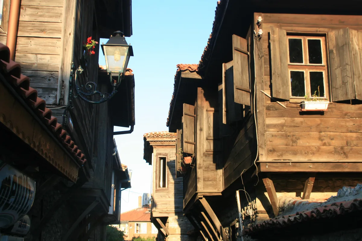 Weathered timber Revival houses in Nessebar old town with overhanging upper floors, a wrought-iron street lantern and geraniums in the evening light