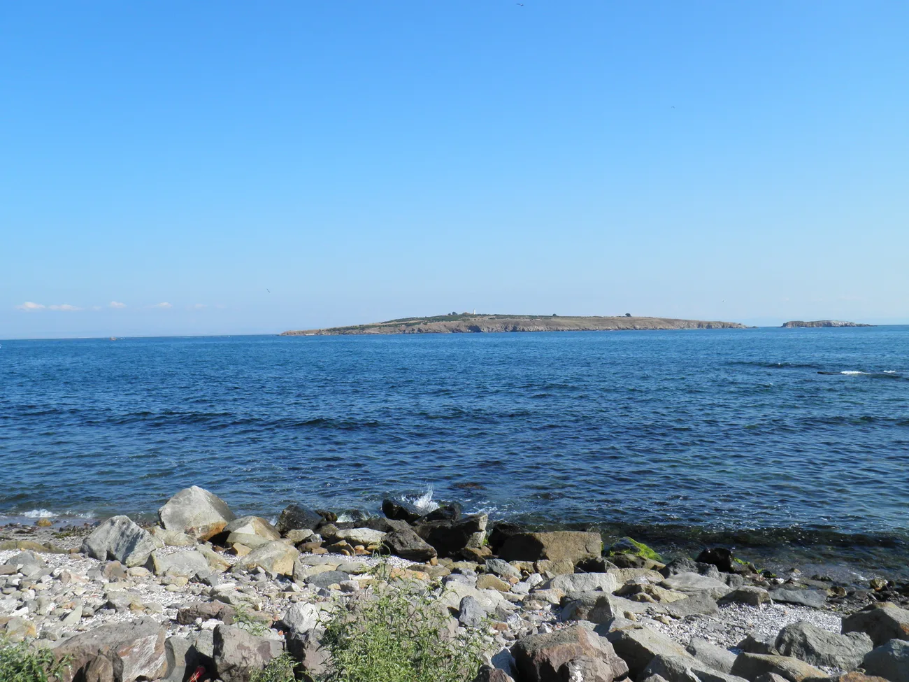 The low green form of St Ivan island seen across the blue Black Sea from the rocky Sozopol shore