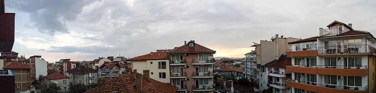 A wide panorama of Nessebar rooftops: red-tiled roofs and houses under a cloudy evening sky