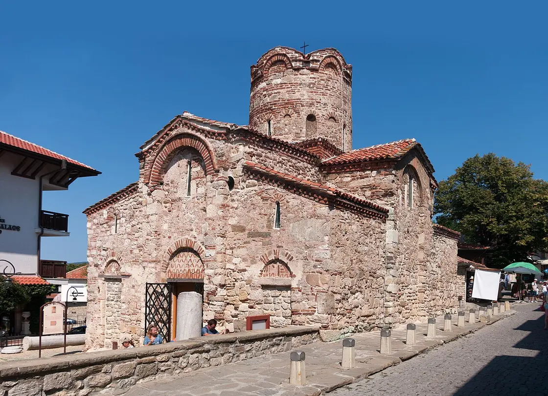 The stone cruciform Church of St John the Baptist in Nessebar with its rounded brick dome, on a cobbled street
