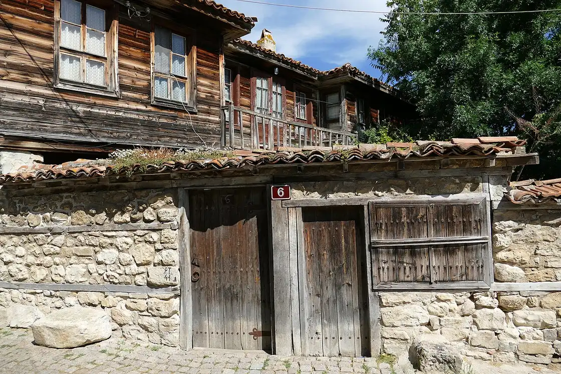 A weathered timber-and-stone Revival house facade in Nessebar with carved wooden doors and shutters marked number 6