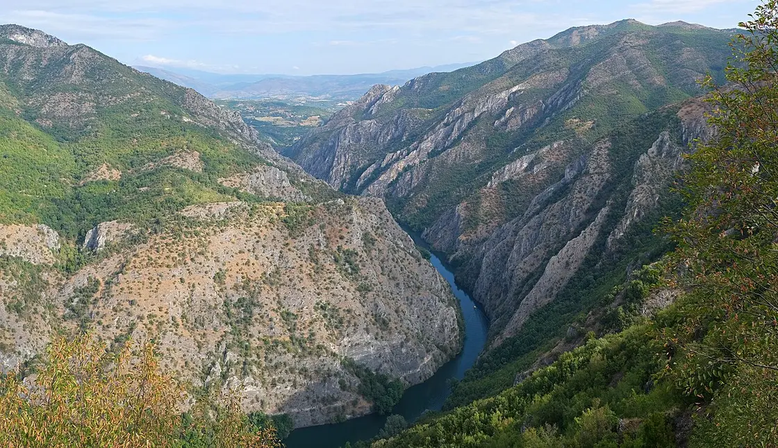 The emerald green water of Matka Canyon near Skopje in North Macedonia, hemmed in by steep forested cliffs and a dam wall