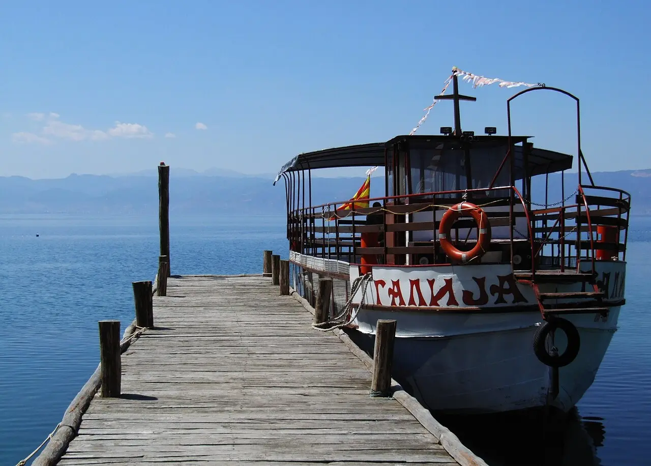A wooden tourist boat named Galija moored on the calm shore of Lake Ohrid with the town and green hills behind