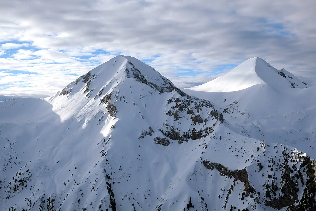 The bare grey rock summits of Vihren and Kutelo in the Pirin Mountains of Bulgaria under a clear sky, with a hiking ridge in the foreground