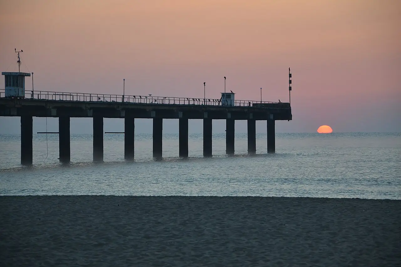 A wide empty sandy beach at Shkorpilovtsi on the southern Bulgarian Black Sea coast at sunrise, with calm surf and a pink sky