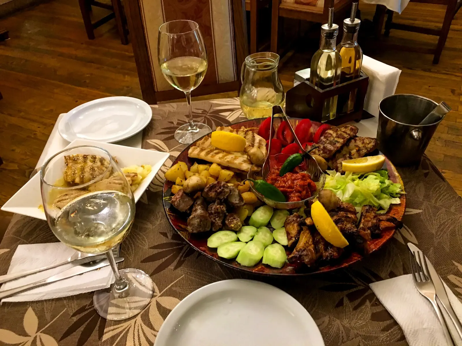 A restaurant table set with a mixed grill platter, glasses of white wine and cutlery