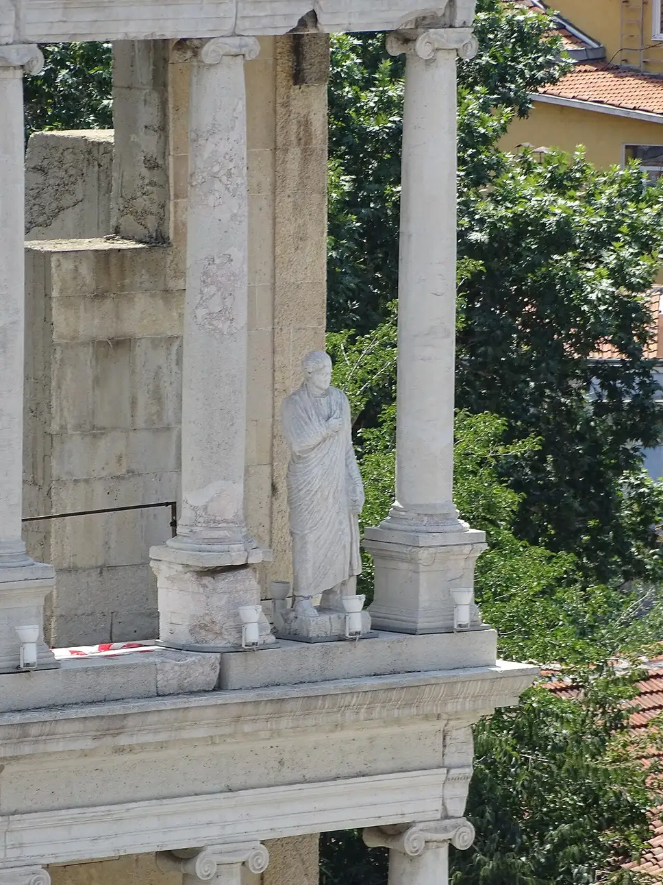 A toga-clad marble statue standing between the Ionic columns of the reconstructed stage building of the Plovdiv Roman Theatre