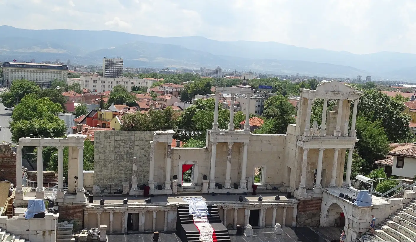 The columned stage building of the Plovdiv Roman Theatre set up for a performance, with Plovdiv rooftops and the Rhodope mountains beyond