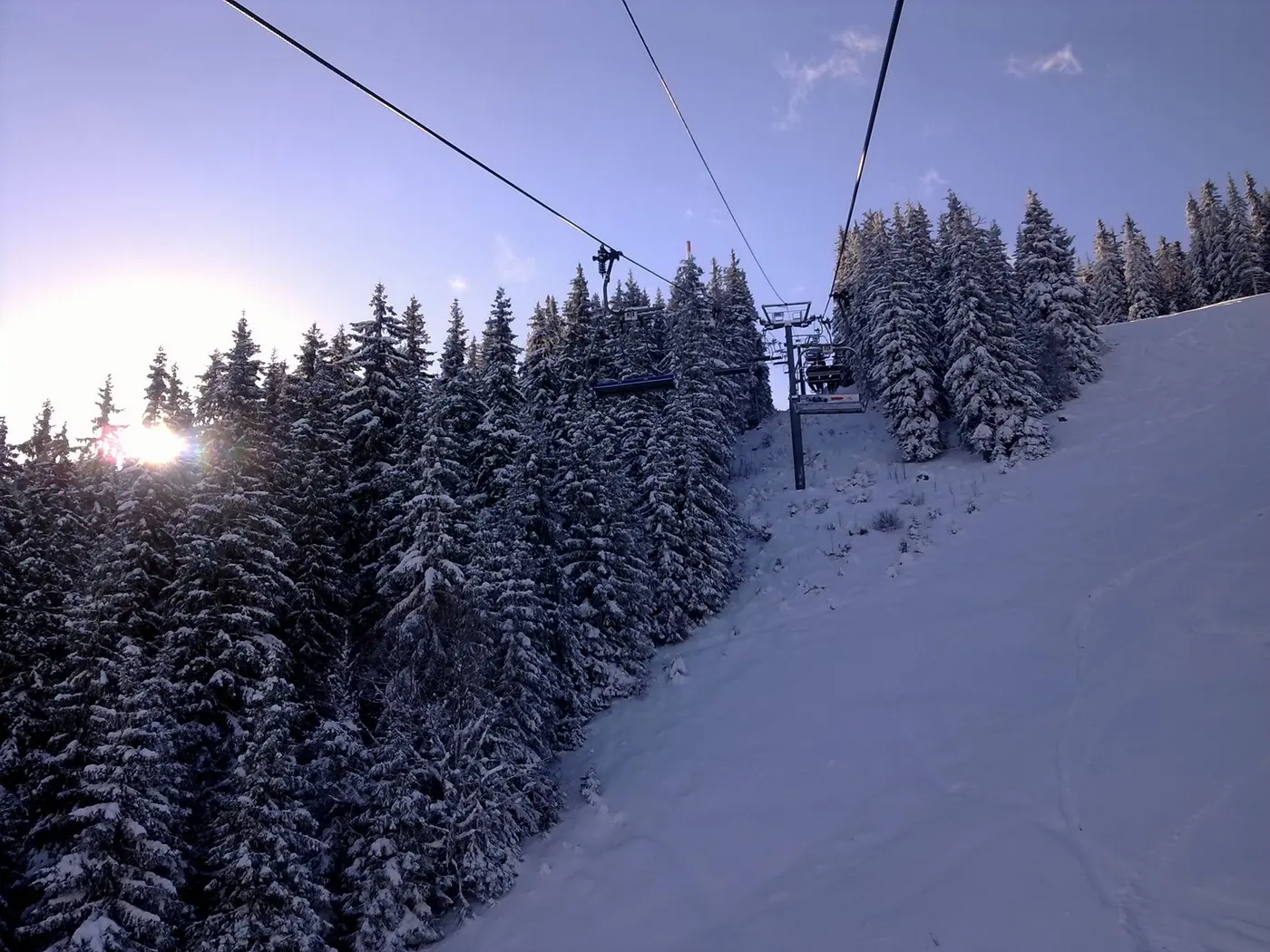 A chairlift climbing past snow-laden spruce trees at Pamporovo in low winter sun