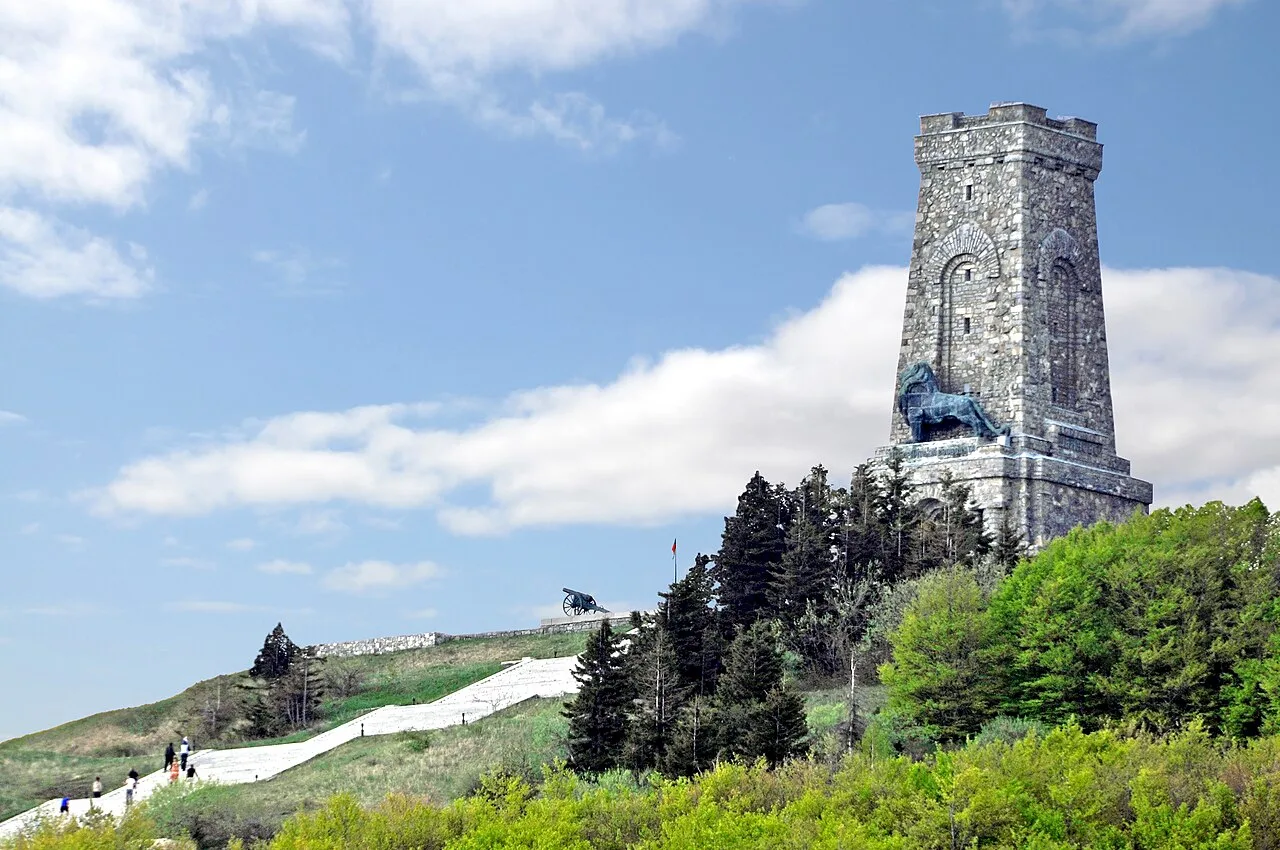 The stone tower of the Shipka Freedom Monument standing on a green ridge under a blue sky