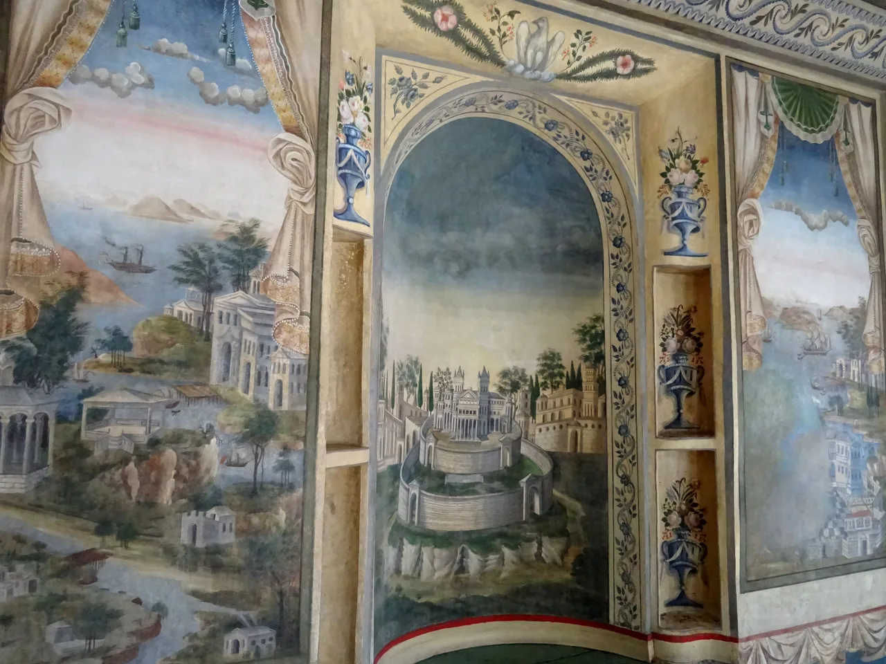 Painted walls in a Revival house room: imaginary harbour towns and a domed city framed by painted curtains and flower vases