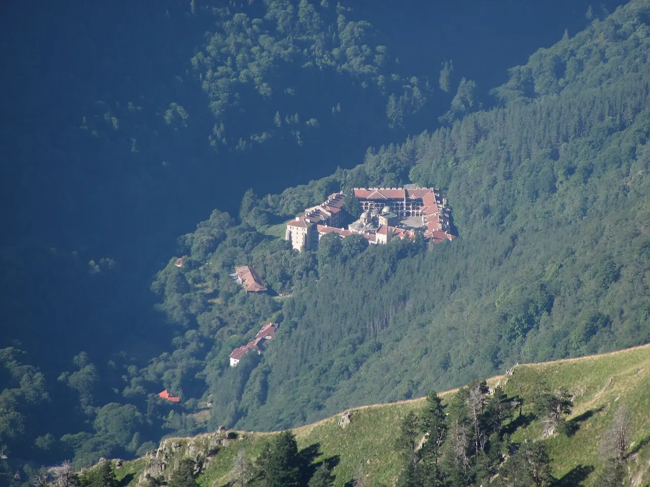 Rila Monastery seen from across the valley, tucked into the forested slopes of the Rila mountains
