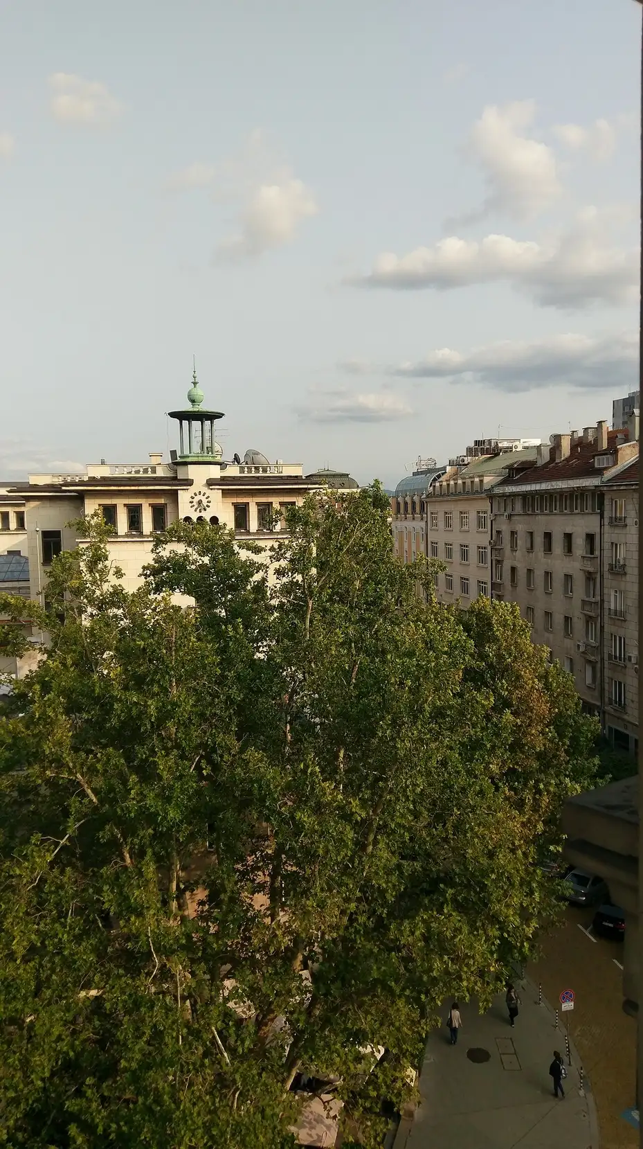 Rooftop view over central Sofia with a historic clock tower and a tree-lined boulevard in evening light