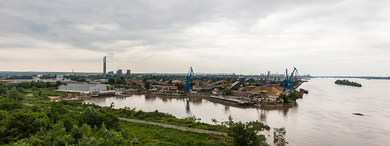 A wide view over the Danube at Ruse with the working river port, cranes and barges, and the flat far bank stretching to the horizon