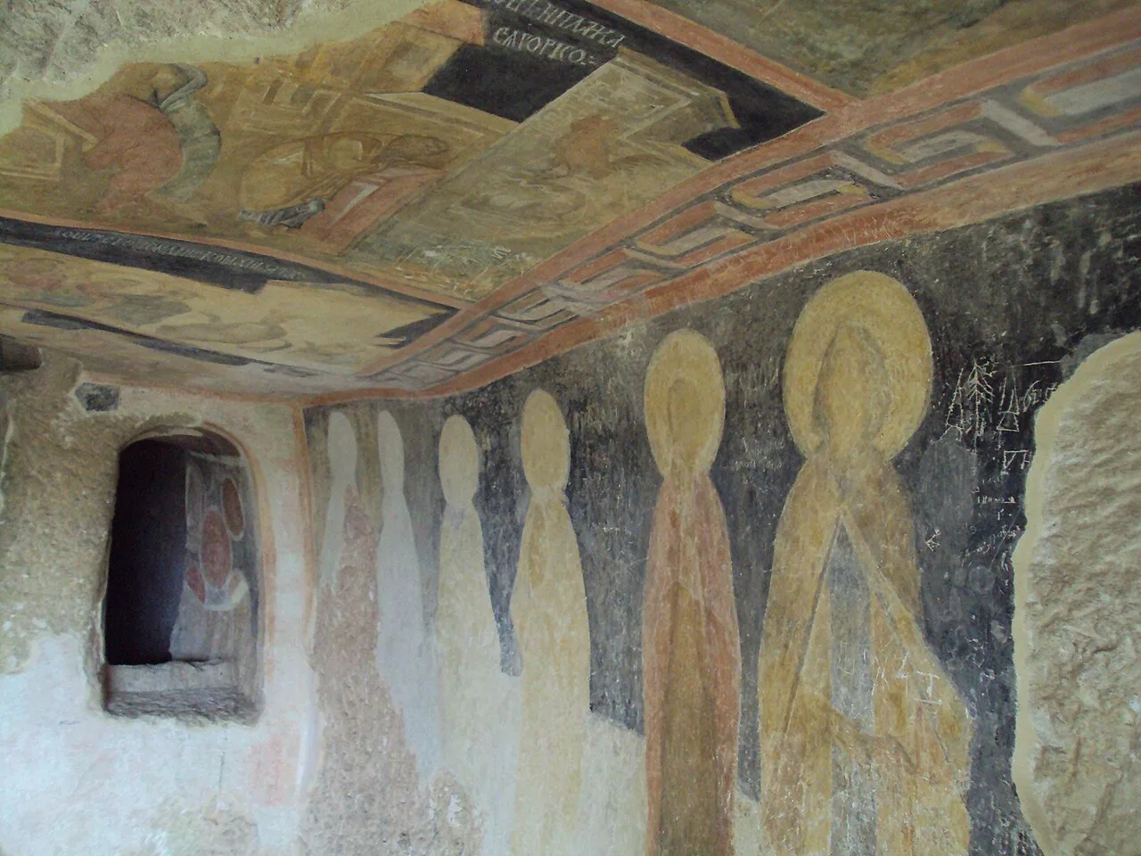A row of haloed medieval saints painted along the rock wall of a church in the Ivanovo complex, with an ornate painted ceiling above