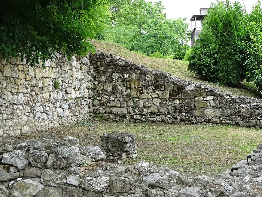 The low excavated stone walls of the Roman fort of Sexaginta Prista in Ruse, on a green slope with a modern viewing tower behind