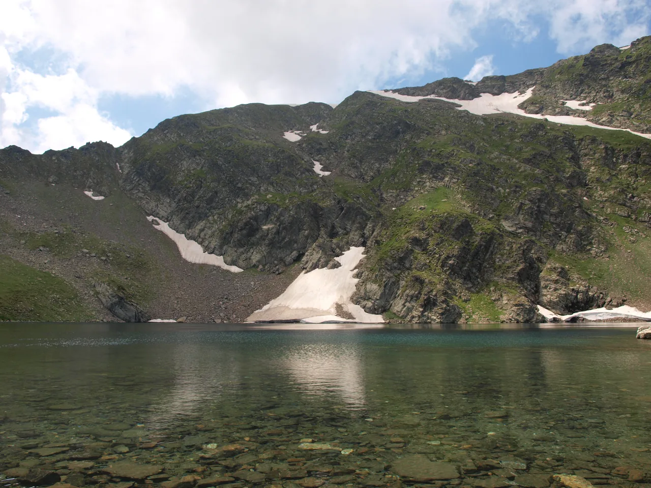 Crystal-clear water of a Rila lake with a rocky cirque wall and a patch of snow behind it