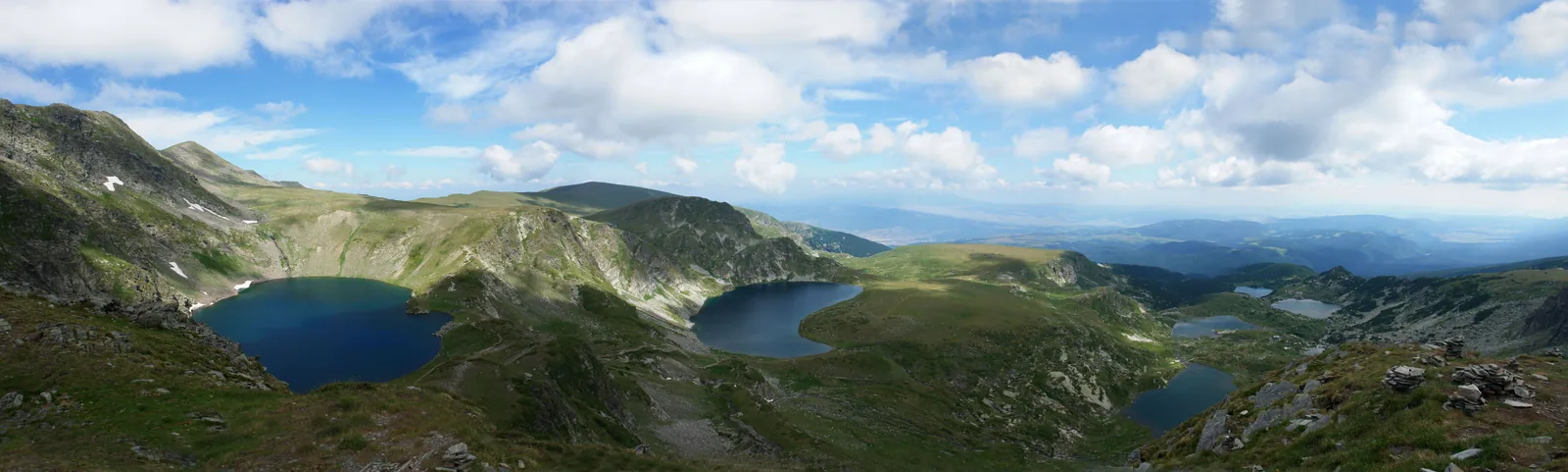 Several of the Seven Rila Lakes seen stacked below a high ridge on a partly cloudy summer day