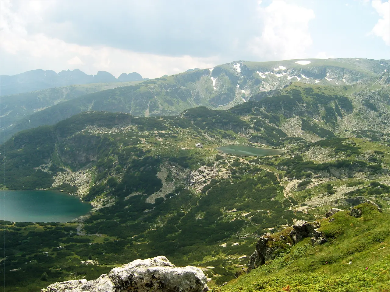 Two of the Rila lakes below a snow-streaked ridge in early summer, with the footpath winding between them