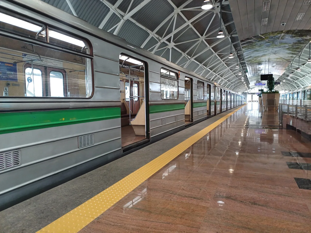 A Sofia metro train with open doors at the Sofia Airport station platform under its curved roof