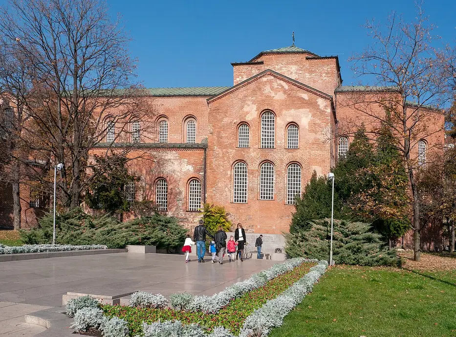 The red-brick basilica of Hagia Sophia in Sofia with its green copper roof, set among trees and a garden