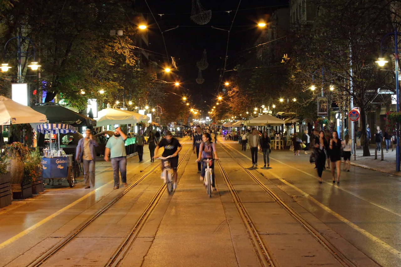 Crowds walking the pedestrianised Vitosha Boulevard in central Sofia at night, cafe terraces lit on either side