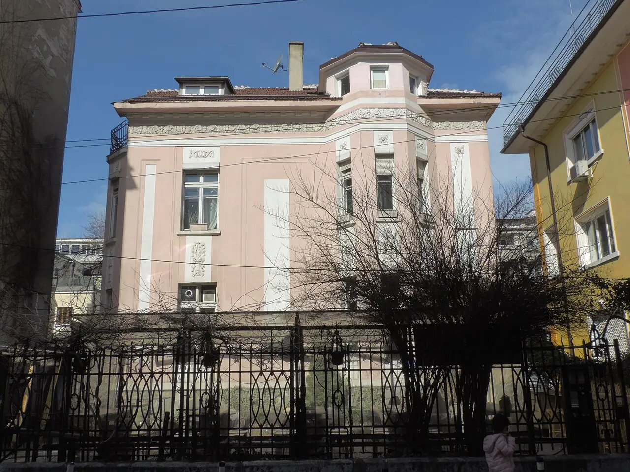 A pink house with a corner turret behind wrought-iron railings and bare trees at 12 Tsar Ivan Shishman Street in Sofia