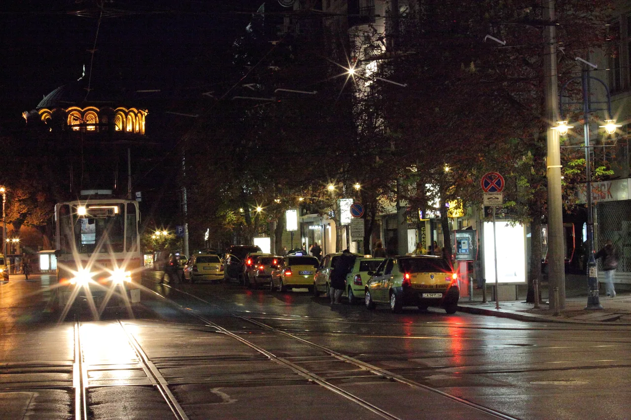 Yellow taxis parked along a Sofia street at night with people on the pavement