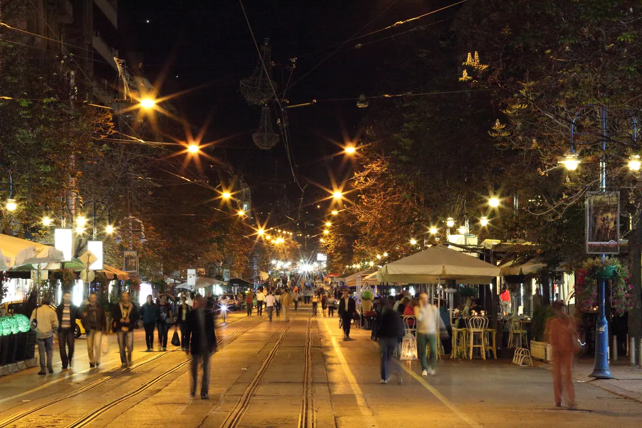 Busy cafe and bar terraces along Vitosha Boulevard in Sofia at night, with people walking under strings of lights