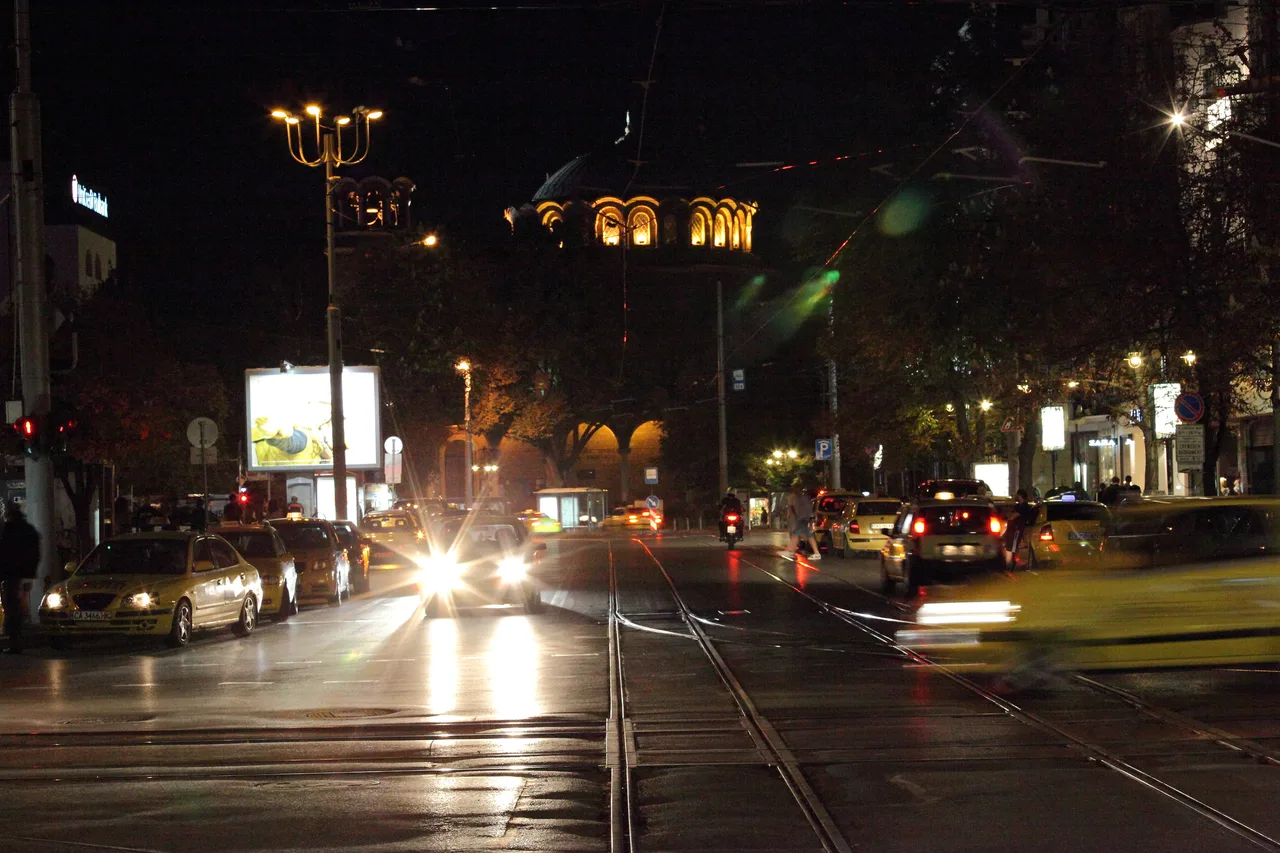 Night traffic on a central Sofia boulevard with a floodlit historic building behind