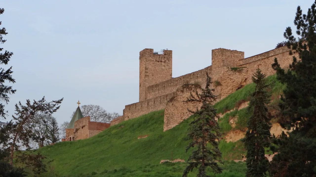 The brick and stone ramparts of Belgrade Fortress (Kalemegdan) on a green hill under a clear sky, with a tower and church spire