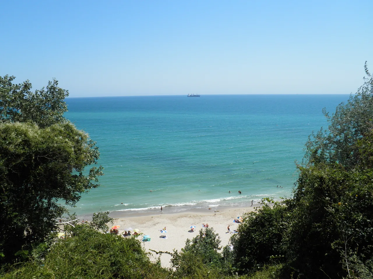 A sandy Black Sea beach in summer with calm water and sunbathers under a clear sky