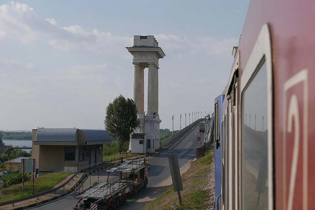 The 1952 stone pylon at the Bulgarian end of the Danube Friendship Bridge with the road deck ramping up and a train carriage in the foreground