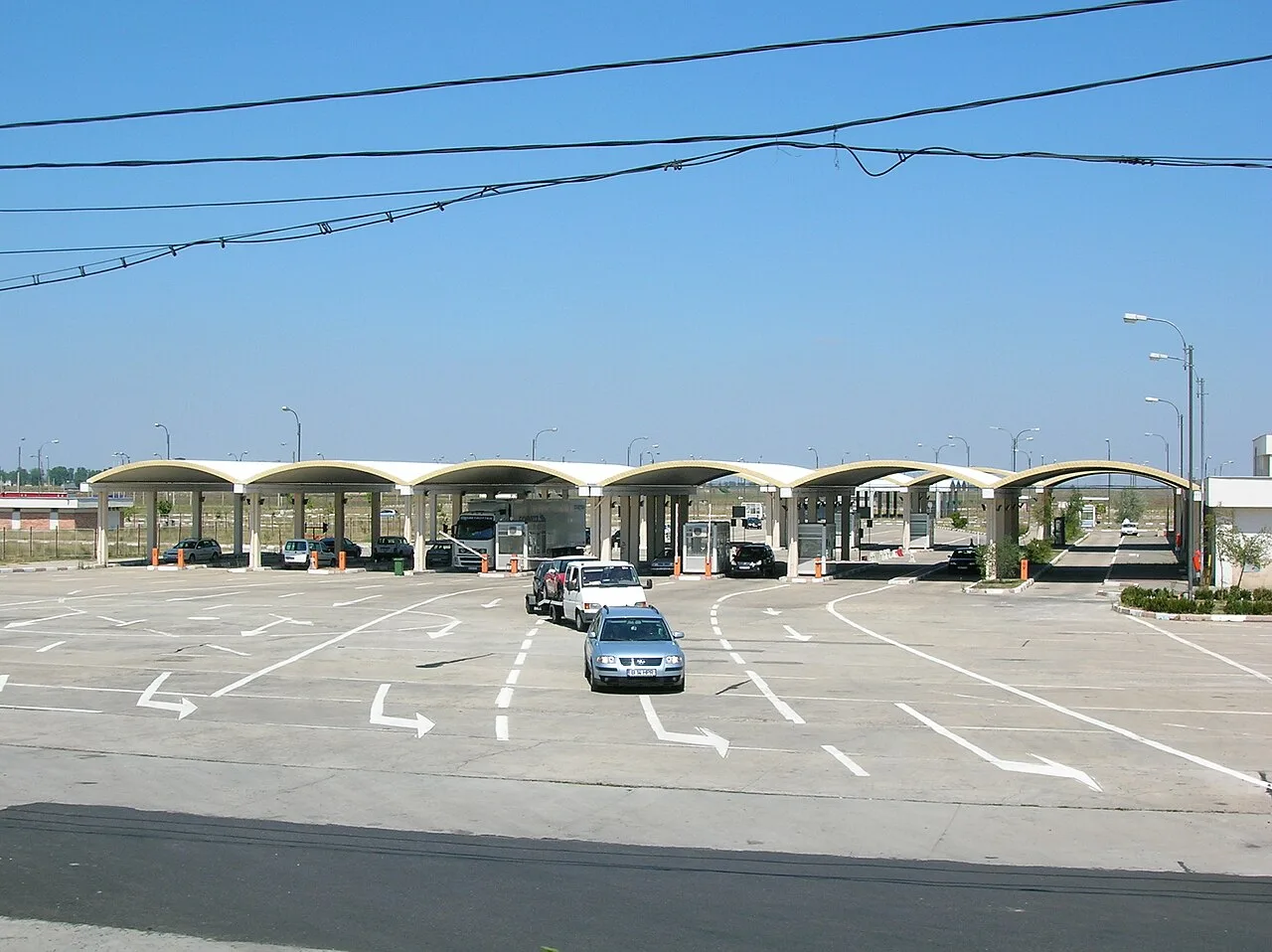 The wide, near-empty canopied lanes of the old border control post at Giurgiu on the Romanian side, with a few cars and overhead wires under a blue sky
