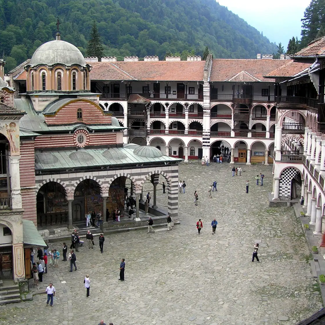 Visitors crossing the cobbled courtyard of Rila Monastery below the arcaded galleries and the church domes