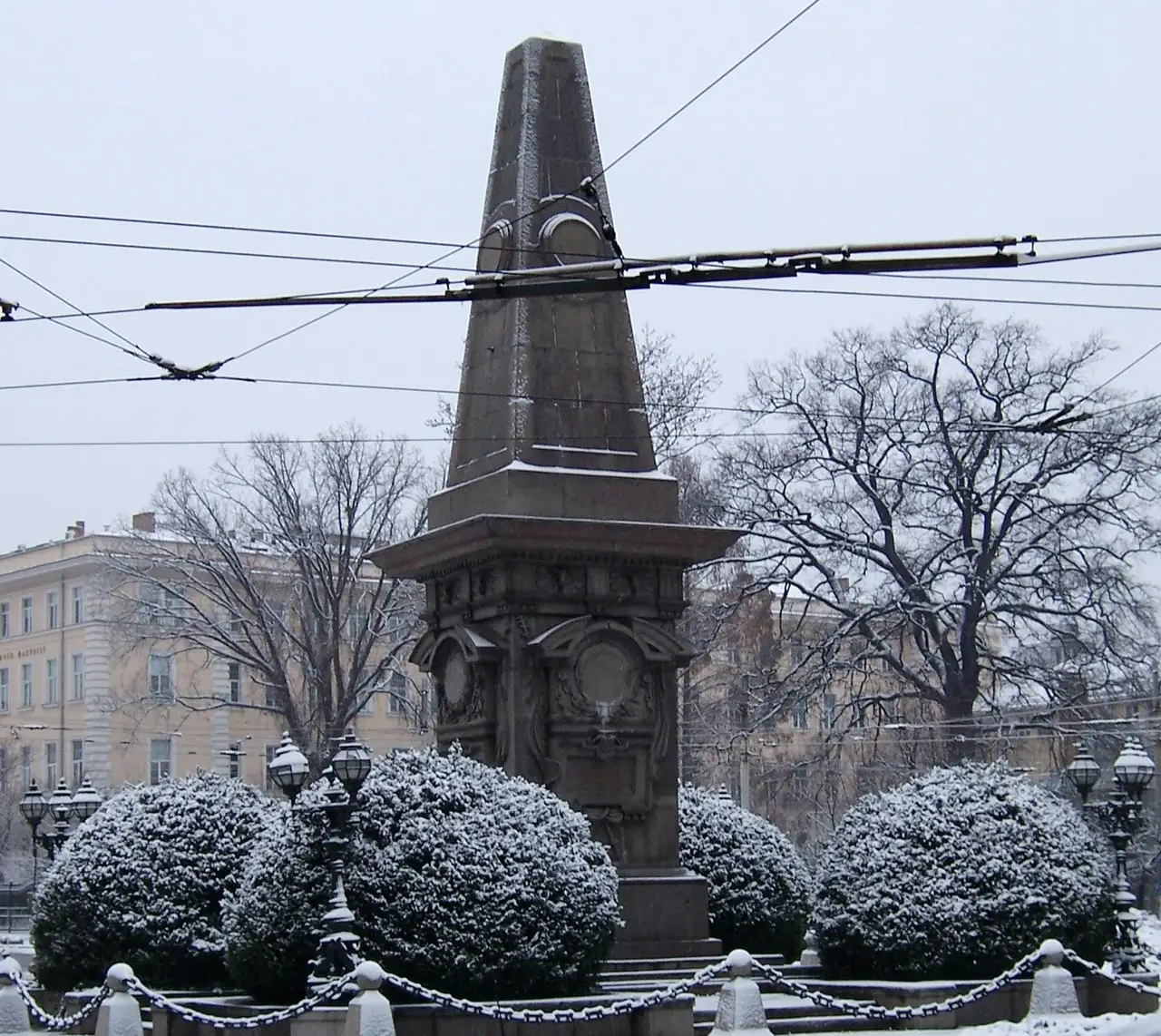 The stone obelisk of the Vasil Levski Monument in Sofia under tram wires on a snowy day