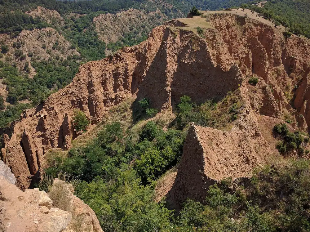Red sandstone spires of the Stob Earth Pyramids rising out of green forest on a hillside