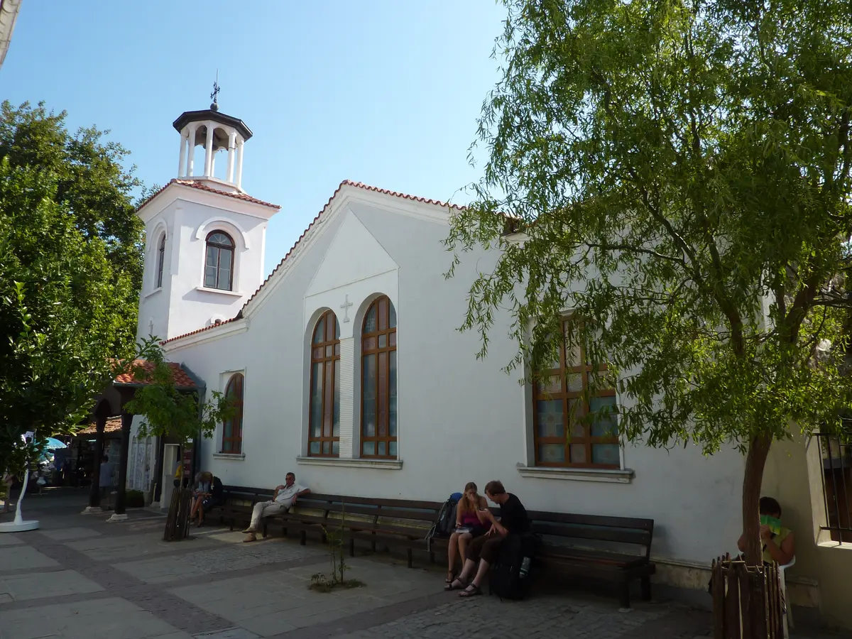 The stone bell tower and tiled roof of the Church of St George in Sozopol old town among trees
