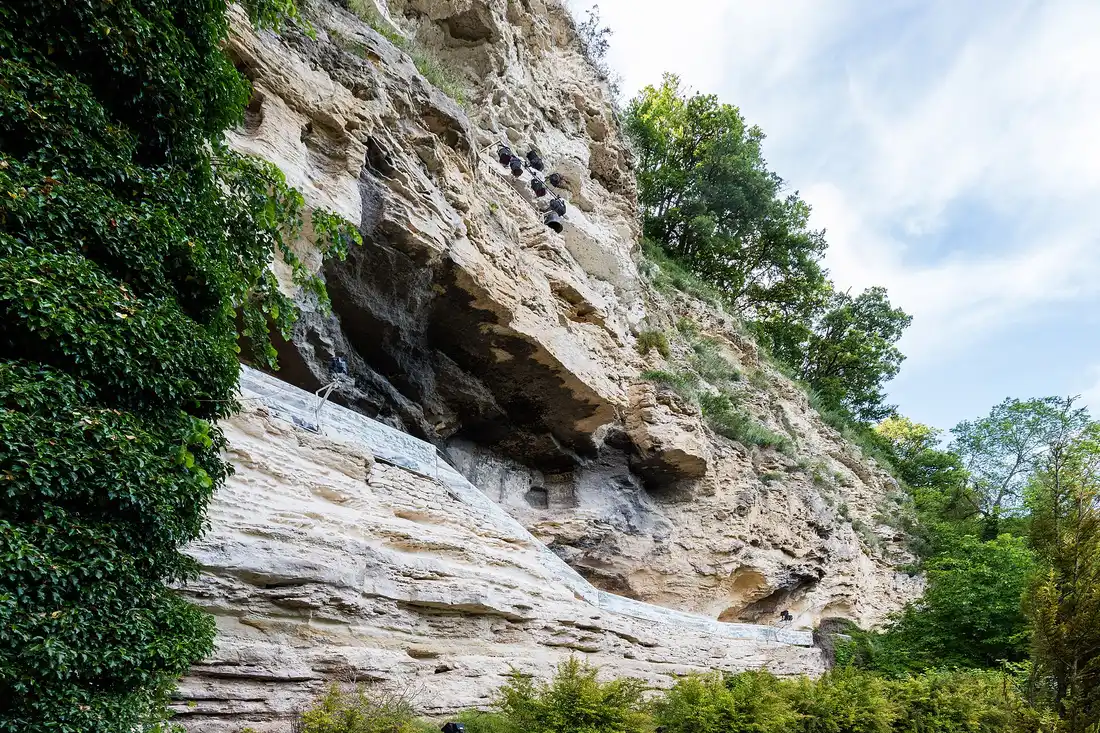 The rock-hewn Aladzha Monastery cut into a sheer white limestone cliff draped with ivy and trees, cave chambers visible high in the rock face