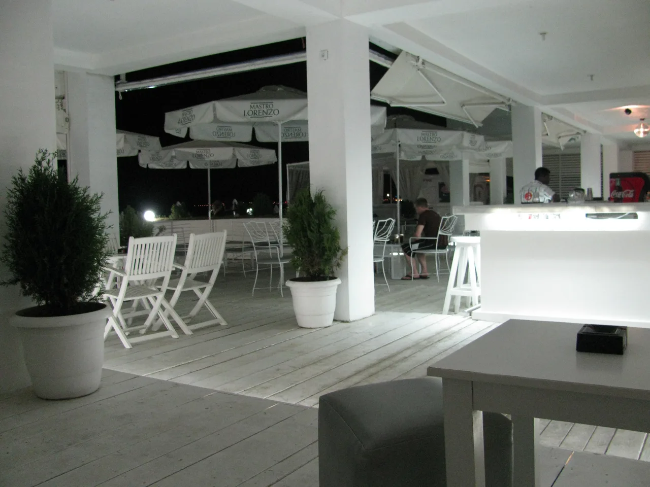 A white-painted beach bar terrace at Sunny Beach after dark, with parasols, bar stools and the sea in the background