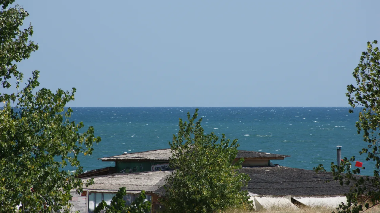 The deep blue Black Sea stretching to the horizon over the thatched roofs of beach bars at Sunny Beach on a windy day