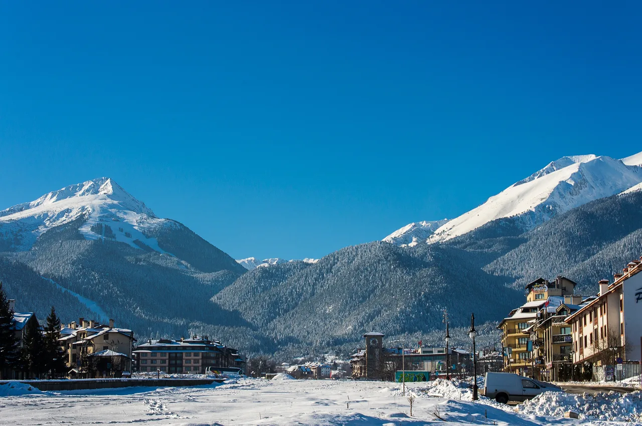 Skiers on a snowy piste at Bansko with the Pirin mountains and a chairlift behind under a clear sky