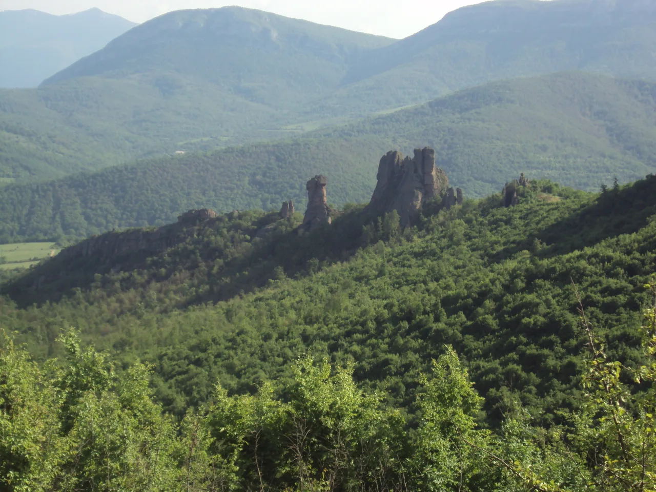 Tall red sandstone rock formations of Belogradchik under a blue sky with green trees at their base