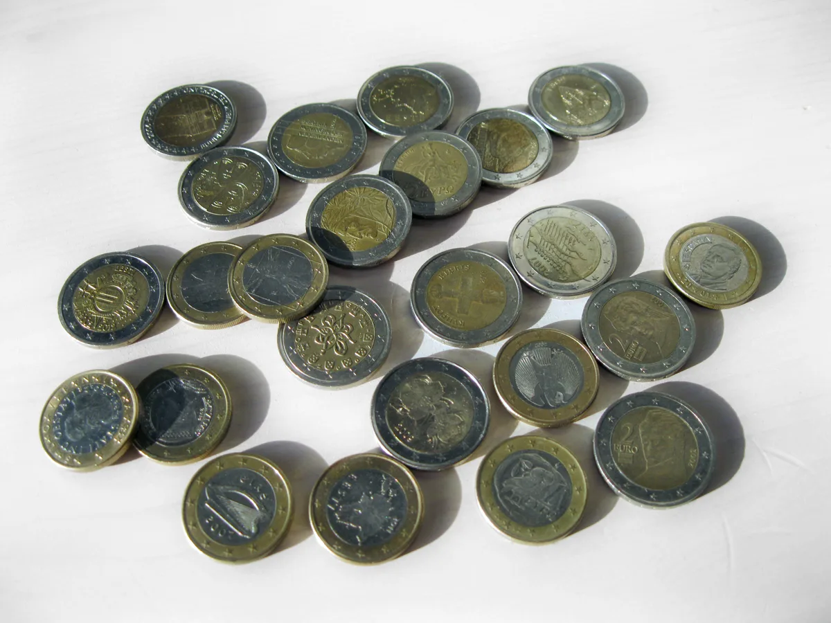 A scattered handful of one-euro and two-euro coins on a white surface